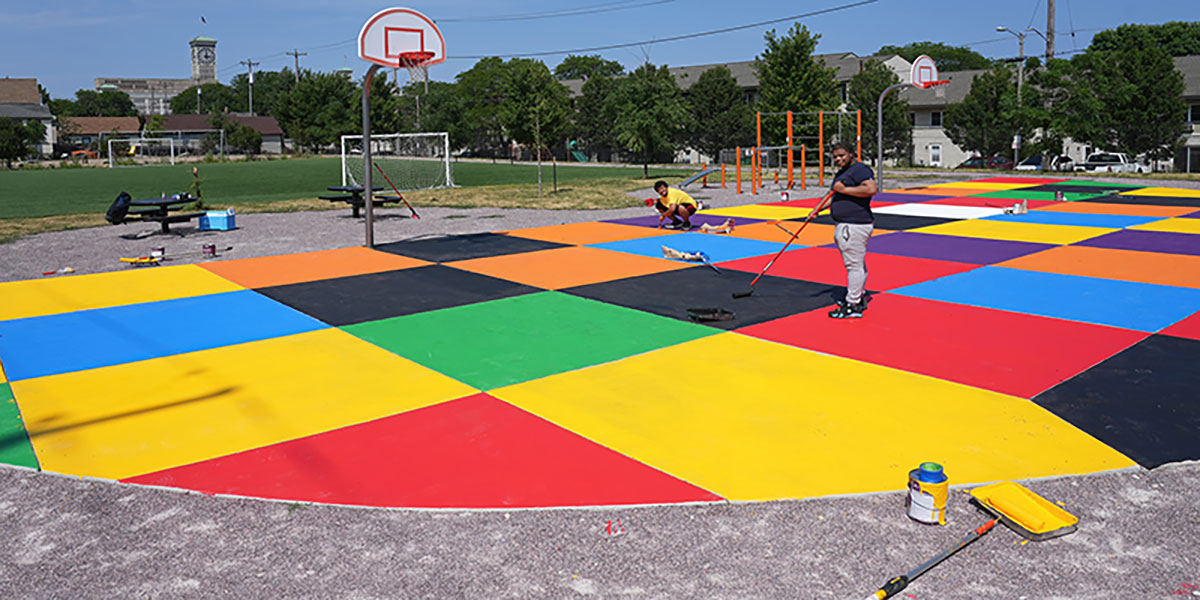 Volunteers painting a colorful geometric mural on a park sports court.